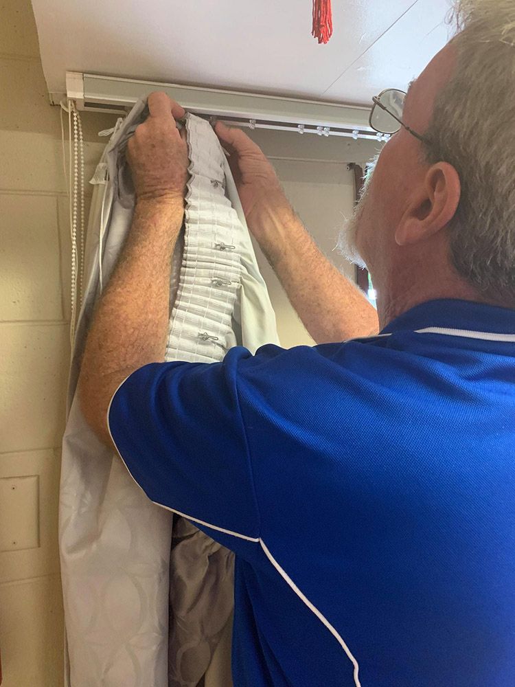 A Man in a Blue Shirt is Hanging Curtains From the Ceiling — Wow Clean Cairns in Palm Cove, QLD