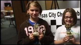 Two girls are holding trophies in front of a sign that says kansas city