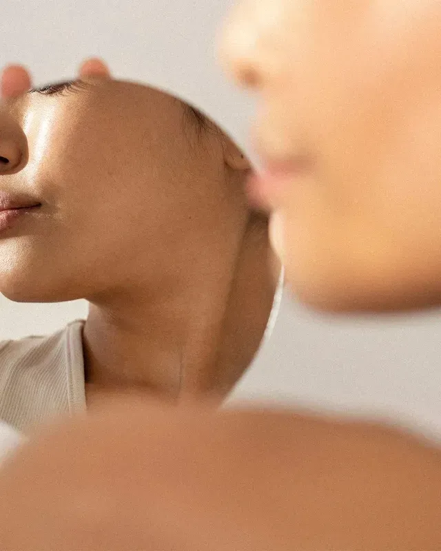 Person looking into a mirror, showing a close-up profile with warm skin tones and a soft blurred background