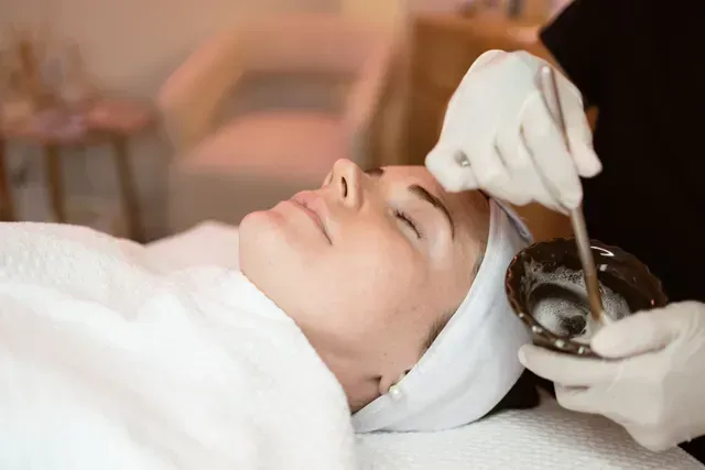 Woman receiving a facial treatment while lying down with a towel wrapped around her head