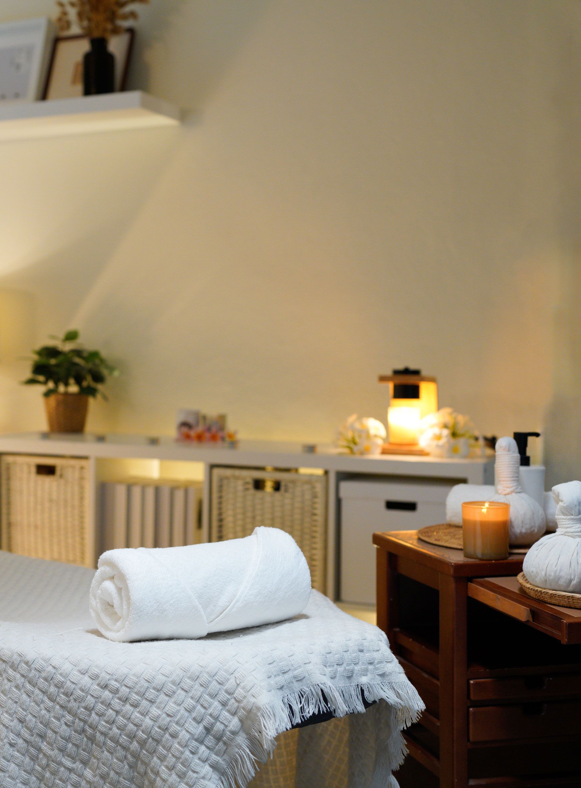 Cozy spa treatment room with massage table, rolled white towel, warm lamp, and wooden storage cabinets