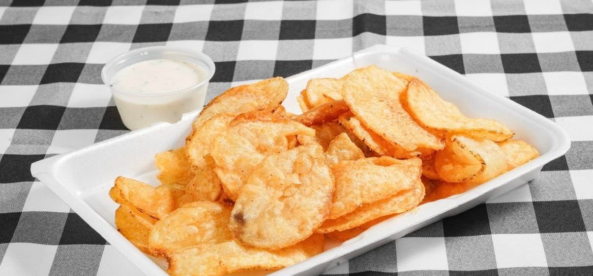 A basket of potato chips with ketchup on a newspaper on a table.