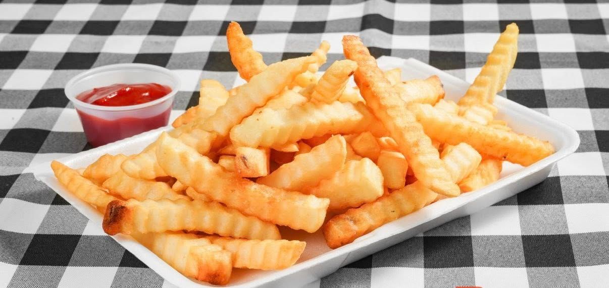 Crinkle-cut french fries in a white container next to a small cup of ketchup, on a checkered table.