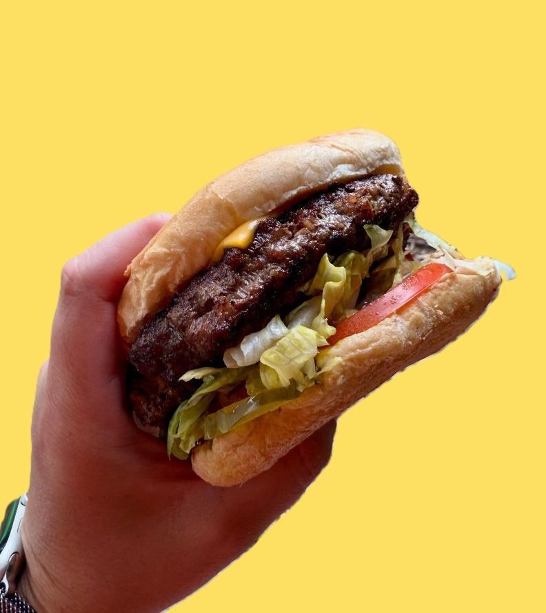 A person is holding a hamburger in their hand on a yellow background.
