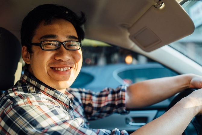 A man wearing glasses is driving a car and smiling.