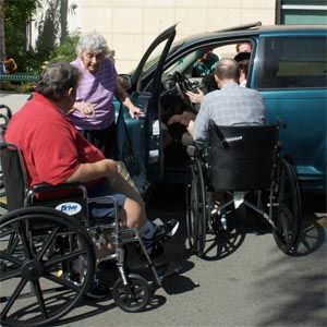 Three people in wheelchairs are getting out of a blue van