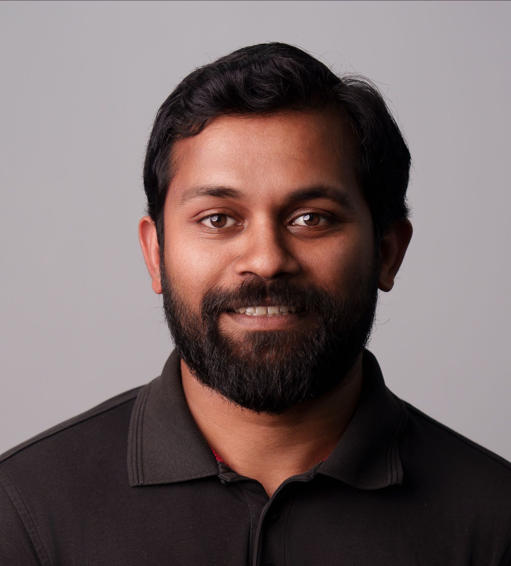 A man with a beard is wearing a black shirt and smiling for the camera.