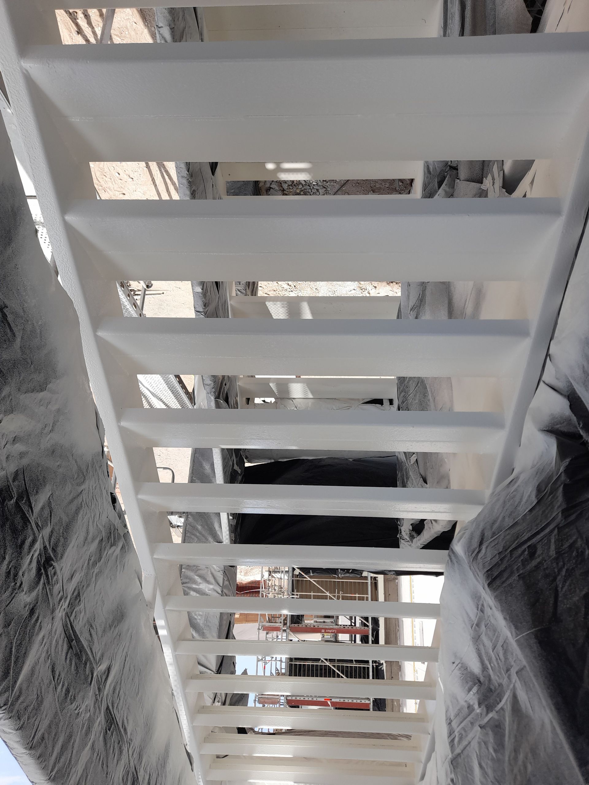 Escalera pintada de blanco desde abajo, con lamas vistas y zonas circundantes cubiertas.