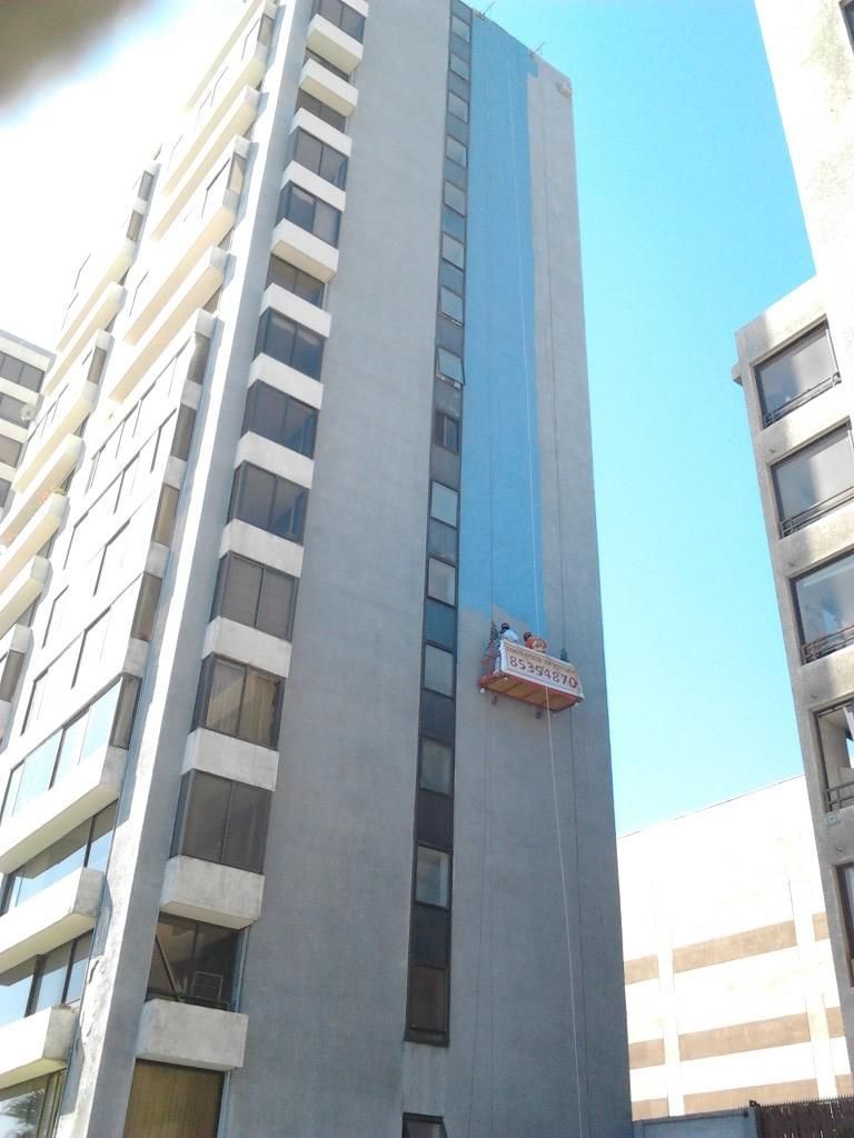 Edificio alto y gris con una sección azul y una plataforma suspendida, bajo un cielo despejado.