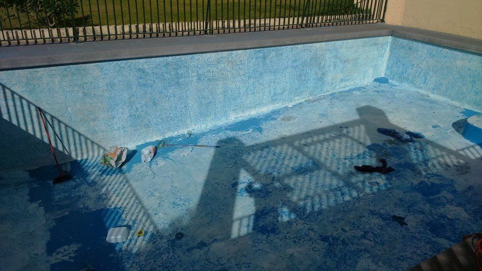 Piscina vacía, pintada de azul, con manchas de agua y residuos visibles, vista desde arriba. 