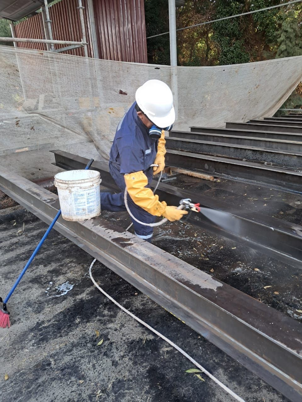 Persona con equipo de seguridad pulverizando vigas metálicas.