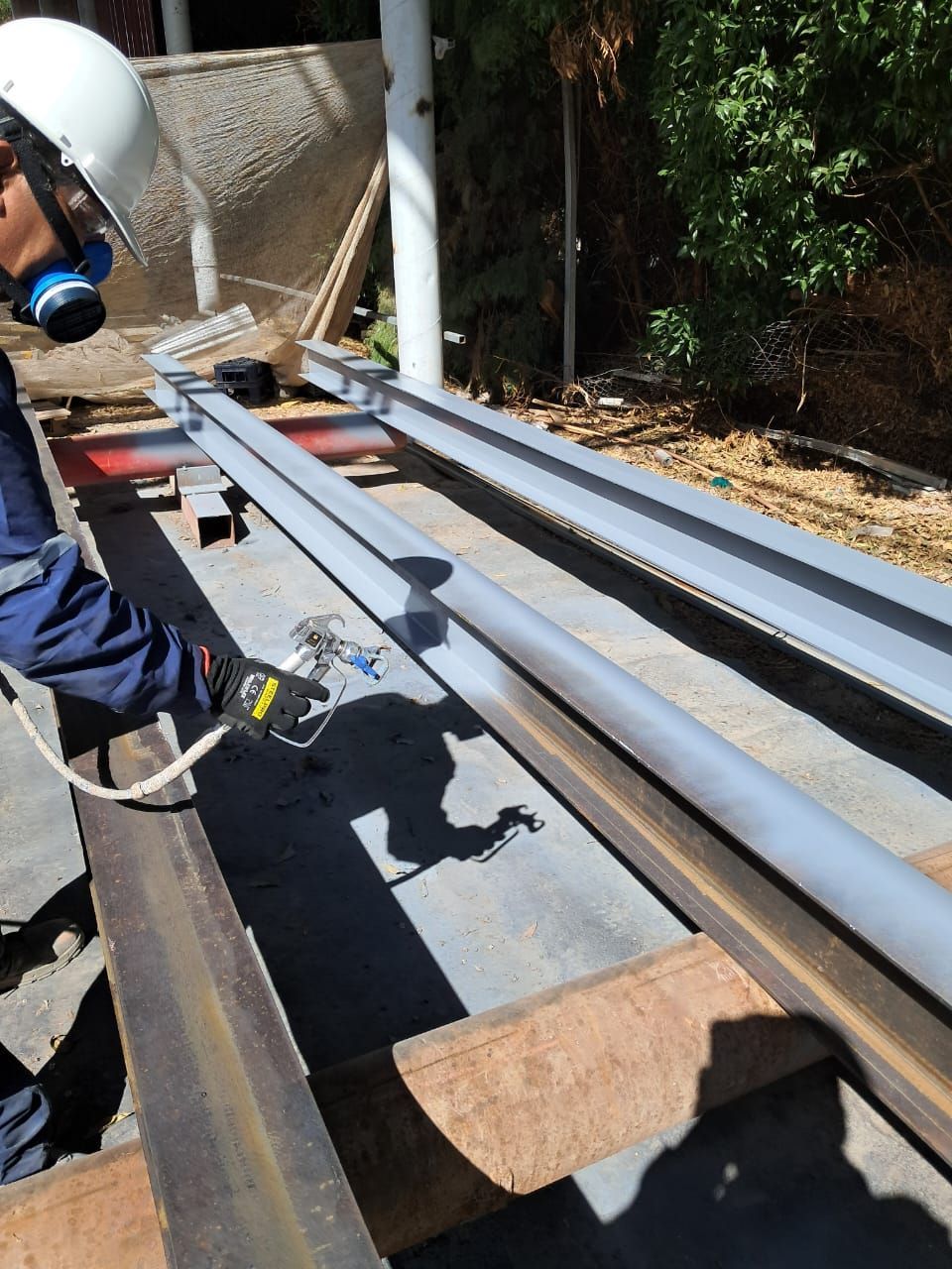 Persona con equipo de protección pintando con aerosol vigas de metal al aire libre.