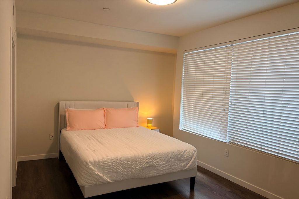 Bedroom with a white bed, pink pillows, and a window with white blinds