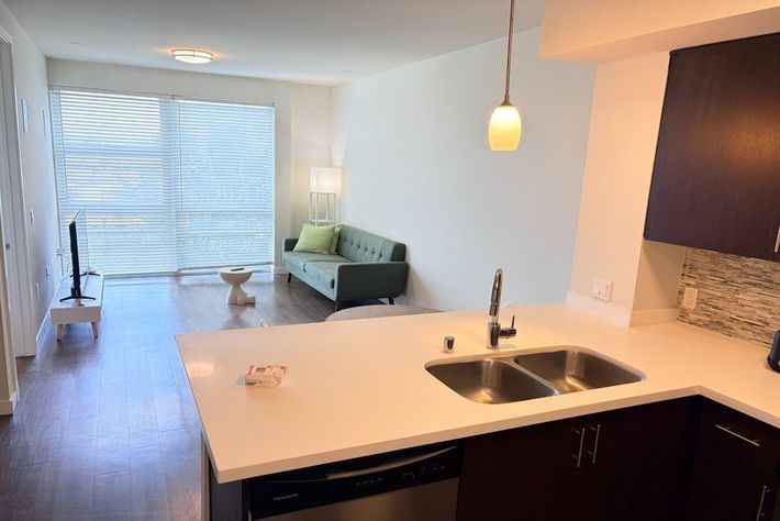 Modern apartment interior with kitchen island, pendant light, sofa, and large window with blinds