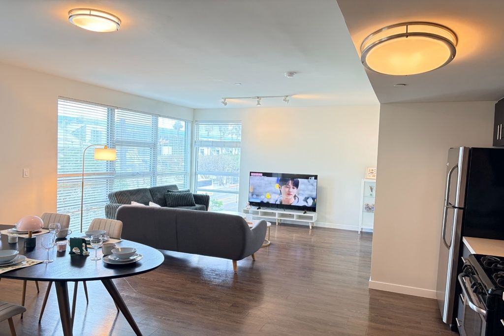 Bright, open living room with gray sofa, TV, dining table, and large windows overlooking snowy trees