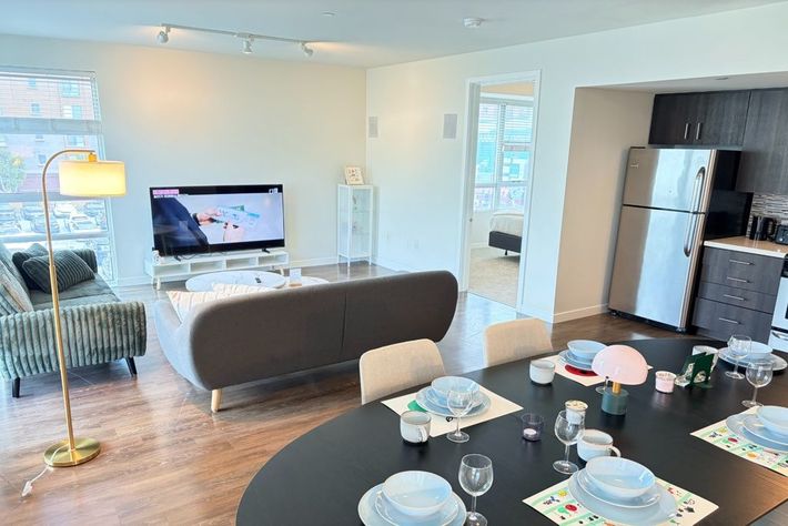 Modern open-plan living room with TV, sofa, dining table set, and kitchen visible