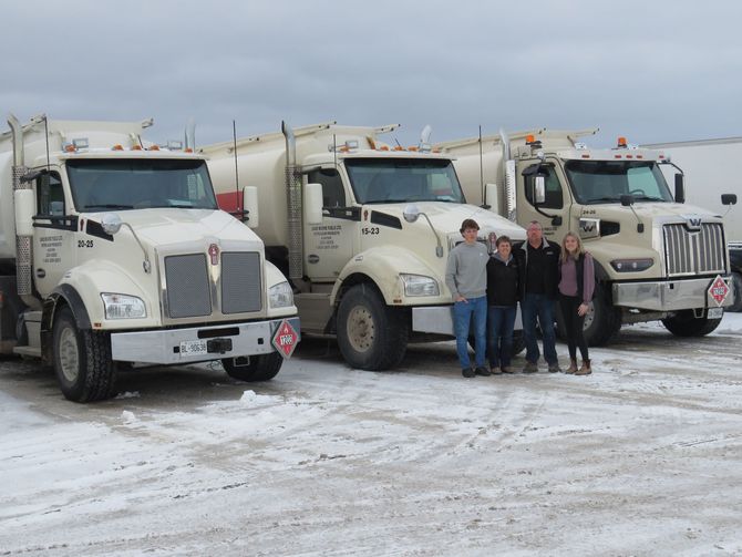 A group of people standing in front of a row of trucks in the snow.