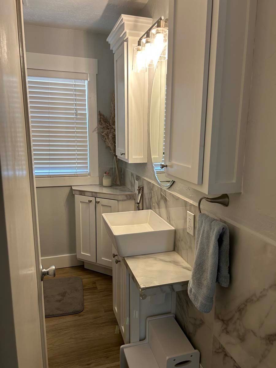 A bathroom with a sink , cabinets , mirror and window.