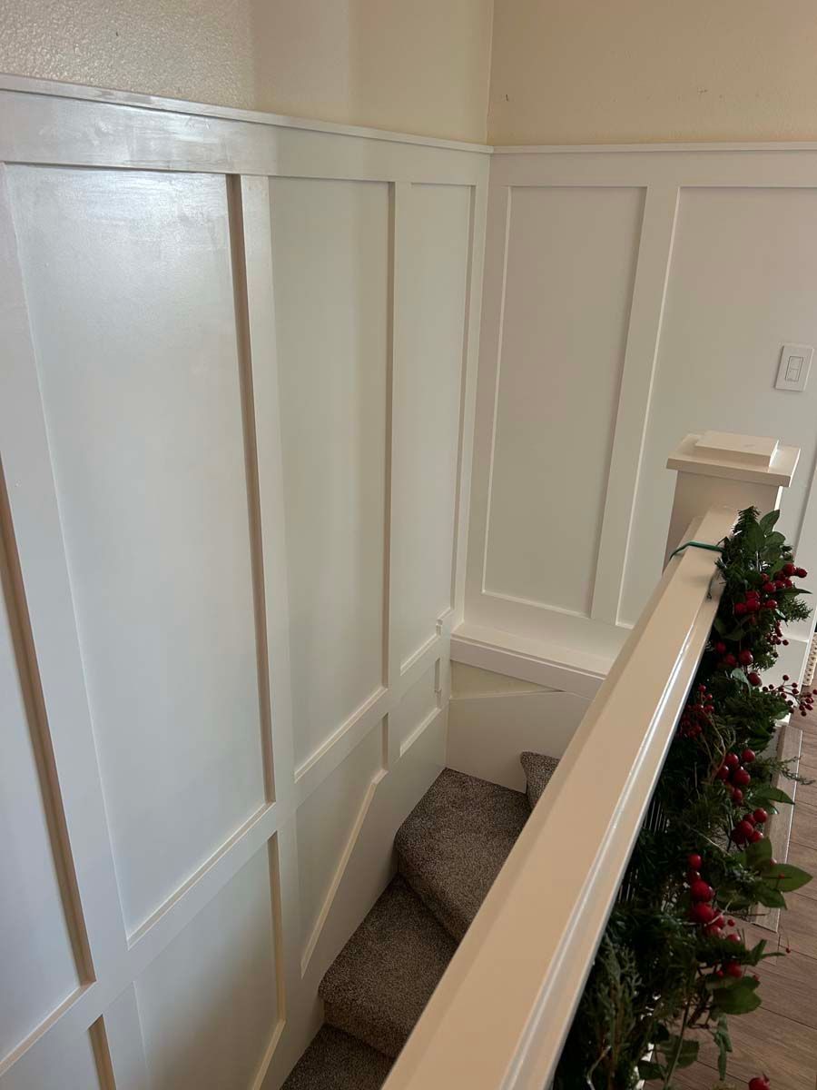 A staircase with white paneling and a christmas tree on the railing.