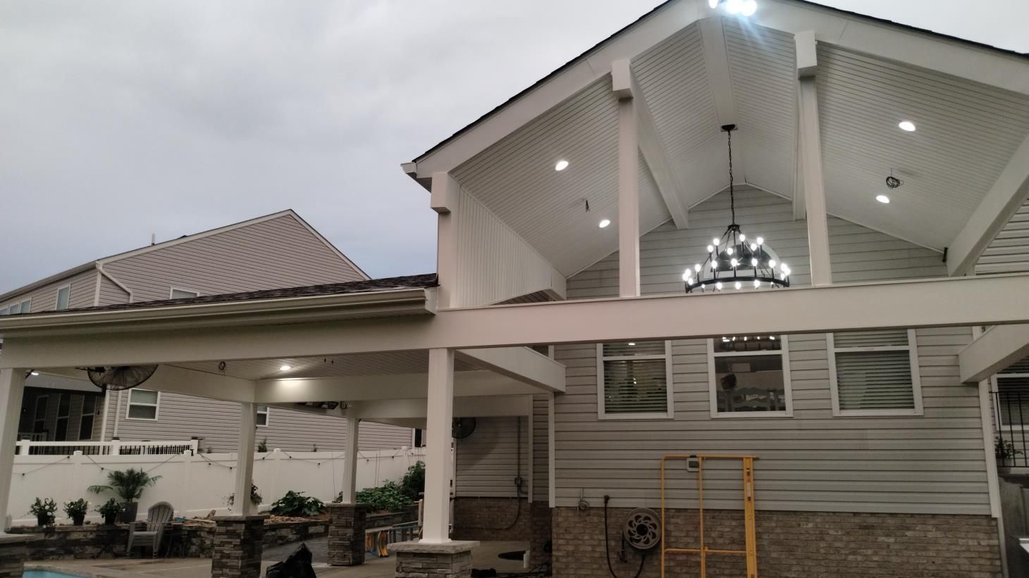 Covered porch and driveway of a light gray house with a white vaulted roof and chandelier lighting.