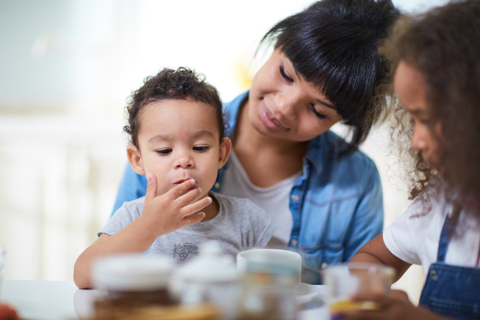 A woman and two children are sitting at a table eating food.