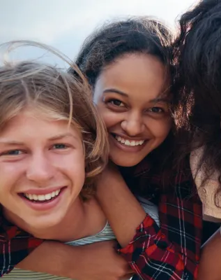 A man is giving two women a piggyback ride and they are smiling for the camera