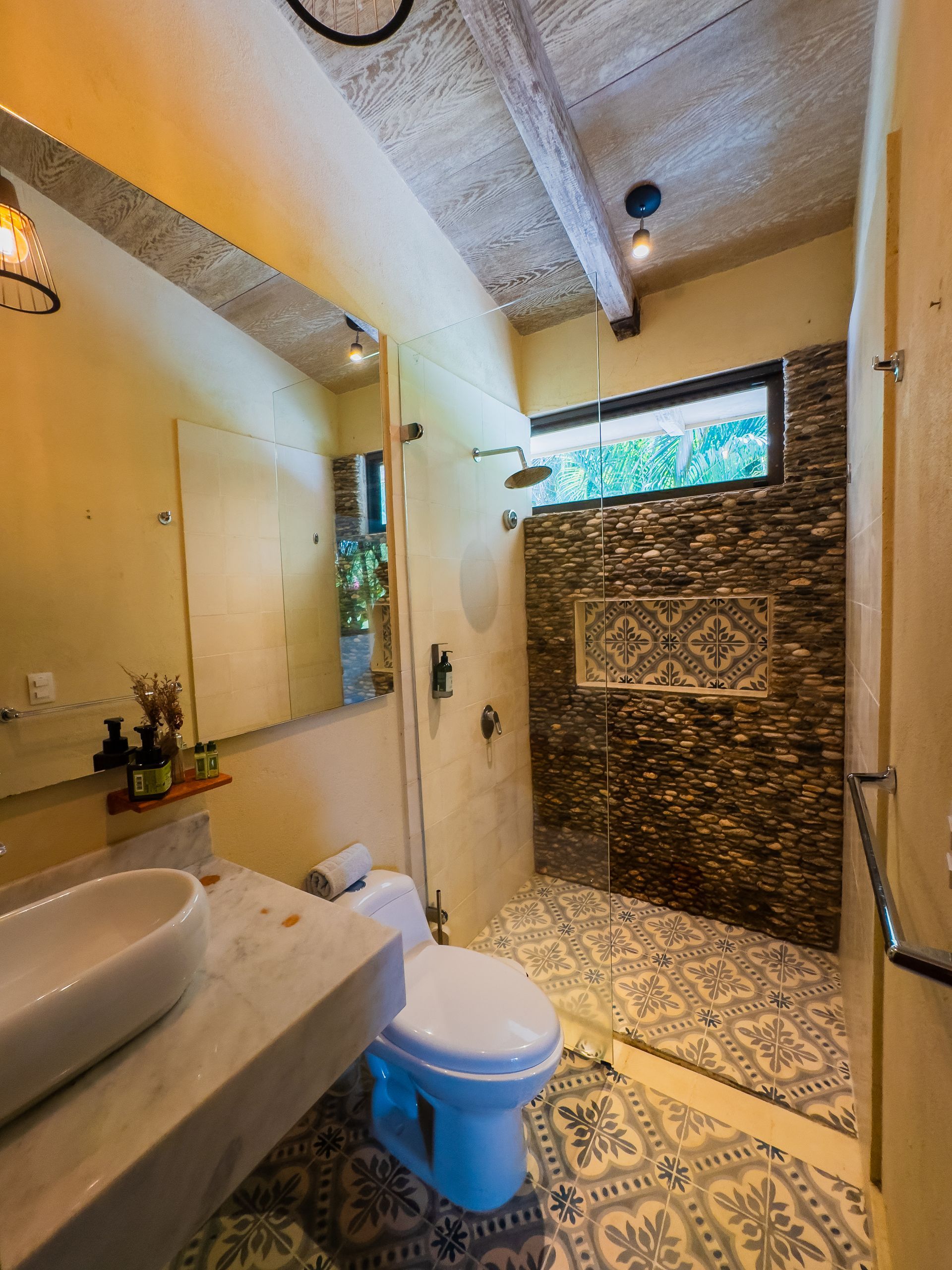 Bathroom with a stone-tiled shower, patterned floor, white toilet, and a vessel sink.