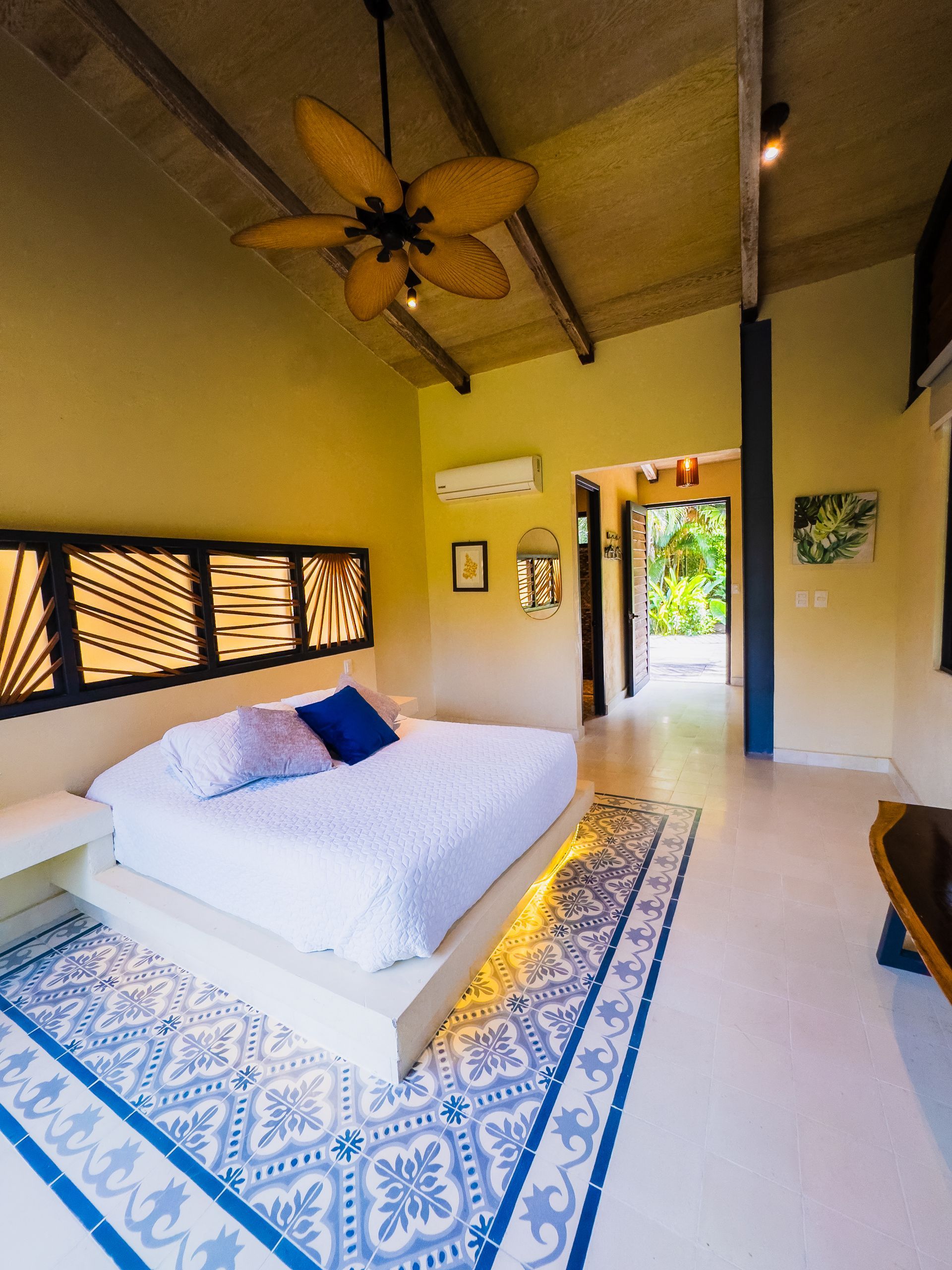 Bedroom with a bed, a blue patterned rug, and a ceiling fan. Pale yellow walls.