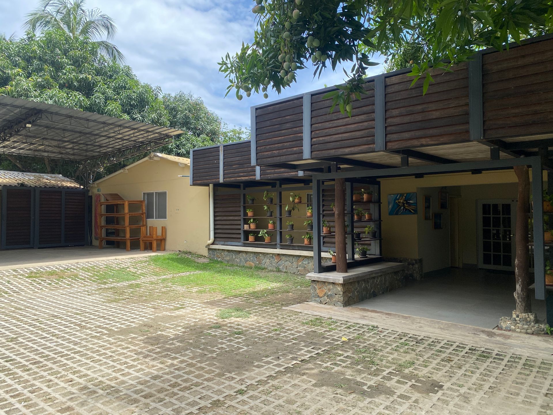 Building with a covered entrance, wooden slats, and a cobblestone-style driveway; surrounded by trees.