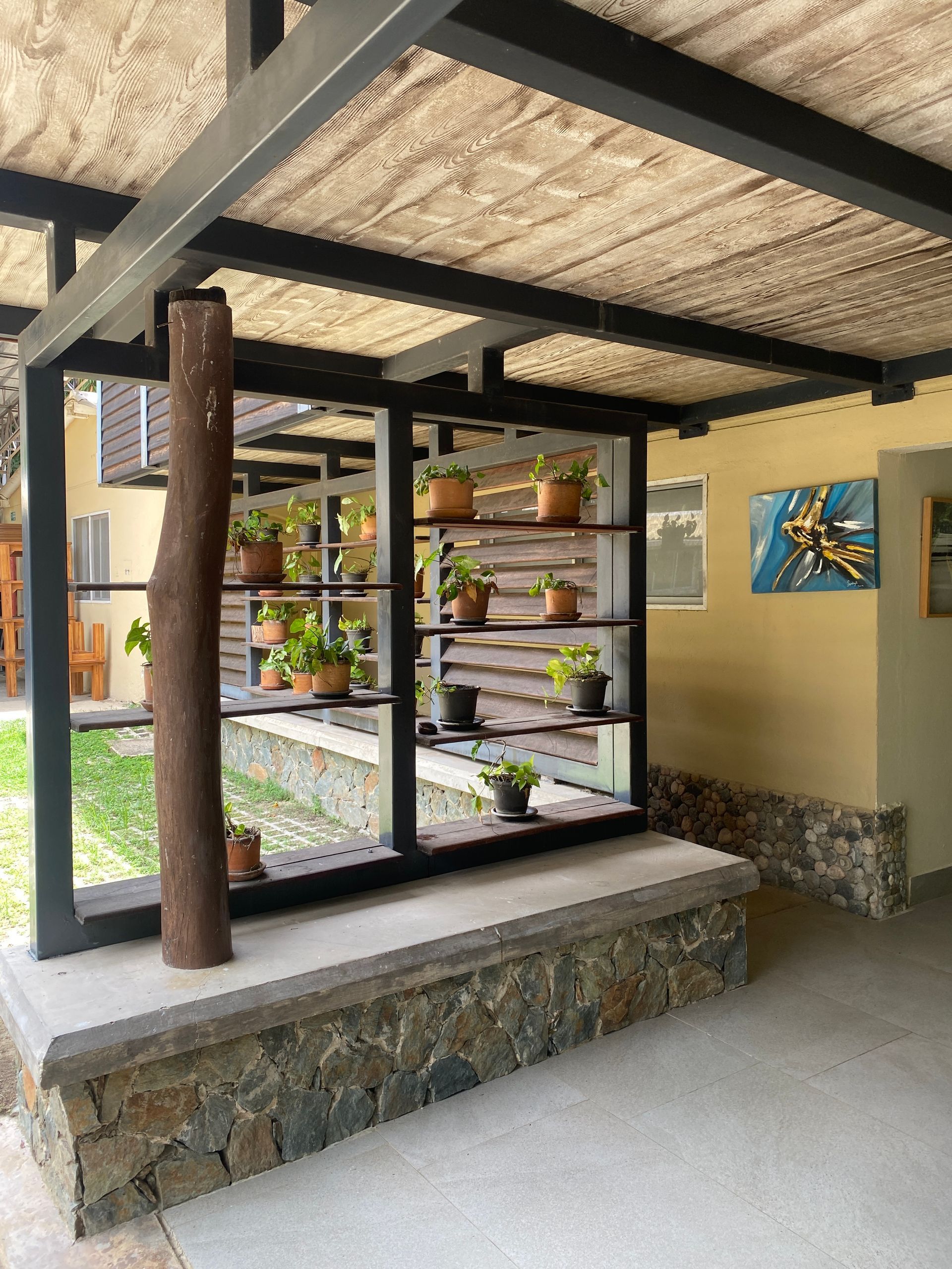 Covered outdoor space with a shelf of potted plants, and stone base.
