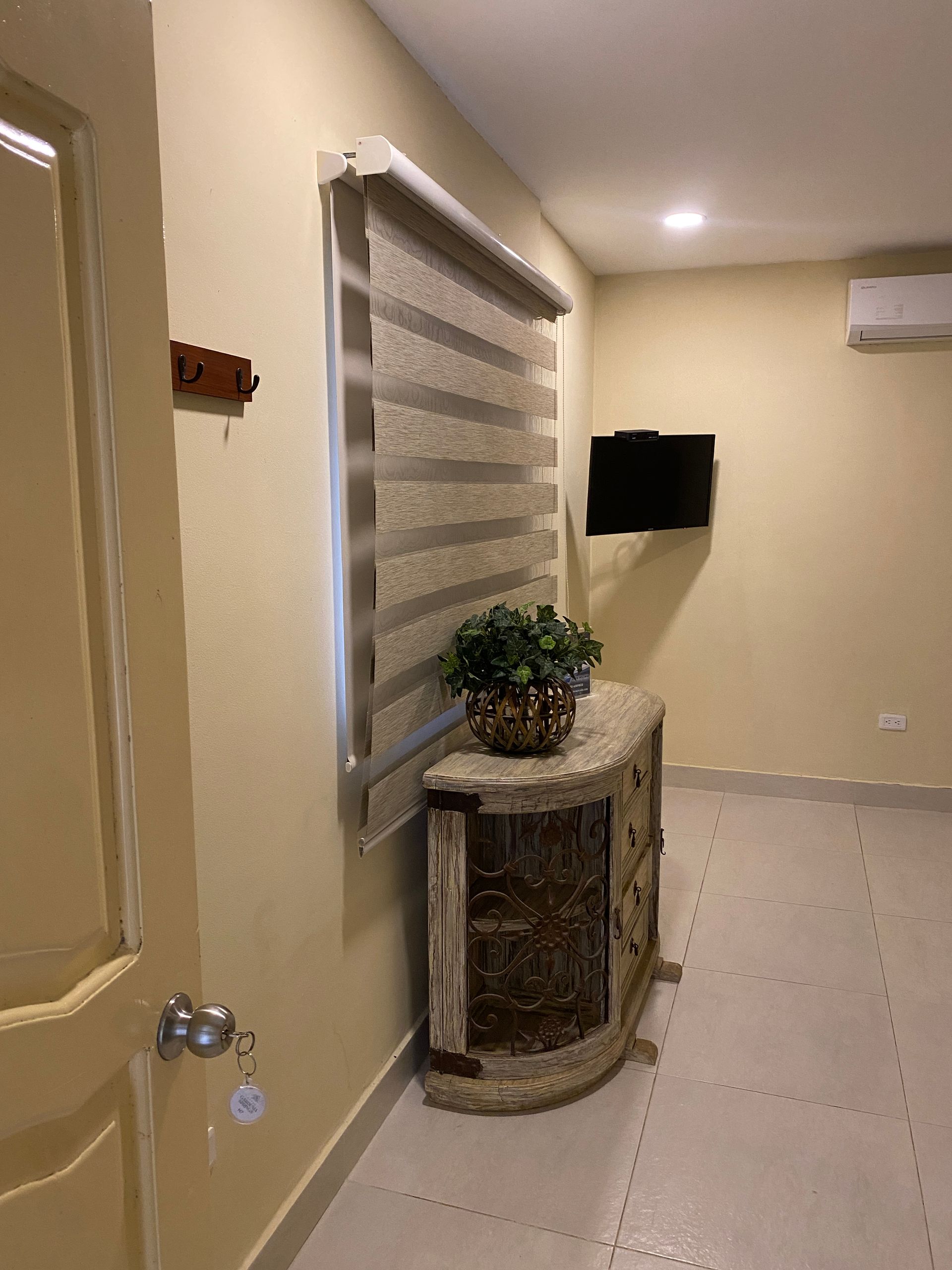 Interior of a room with a decorative cabinet, TV, window with blinds, and a door.