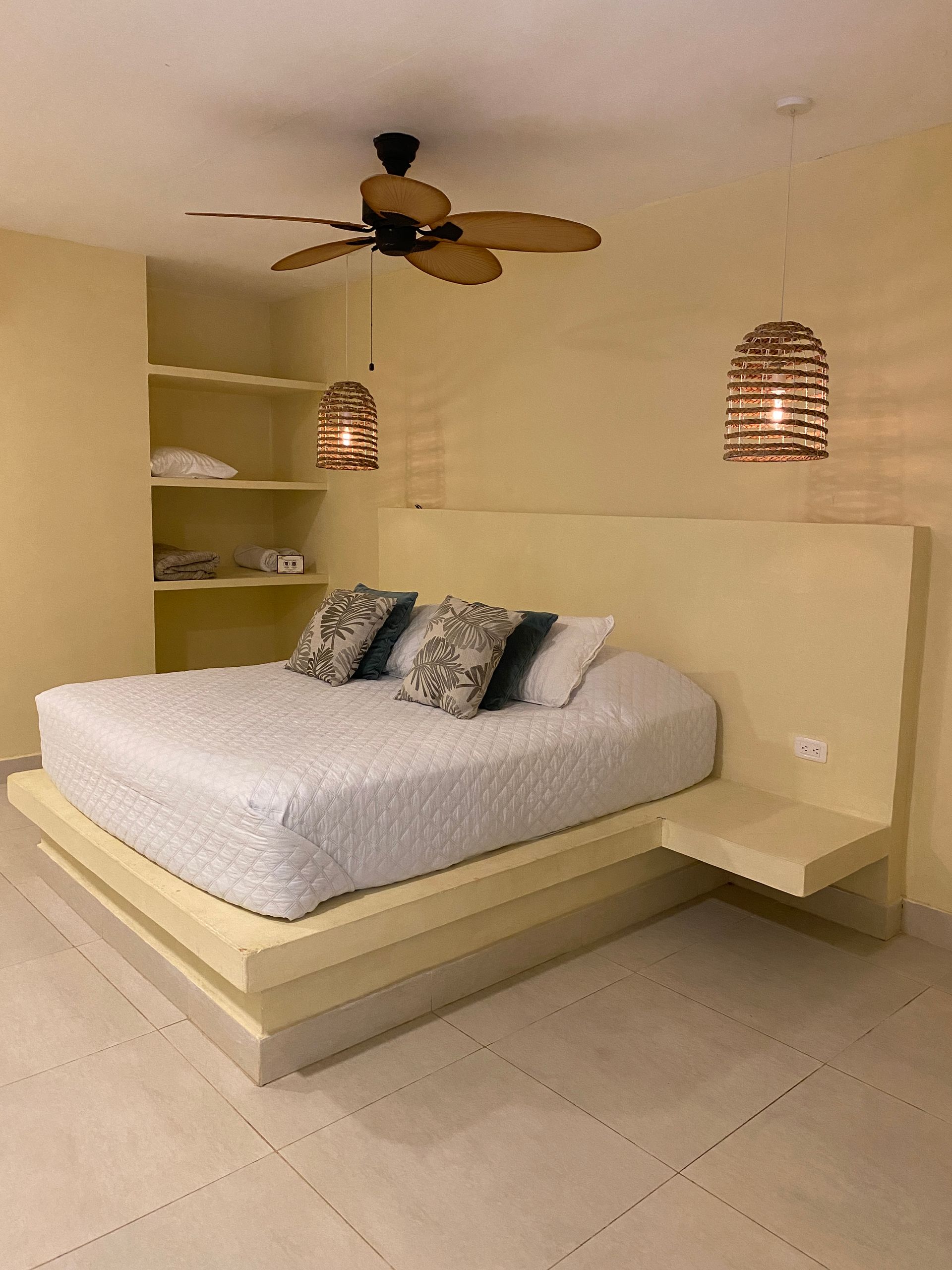 Bedroom with a light yellow built-in bed frame and headboard, matching shelves, and two hanging woven lamps.