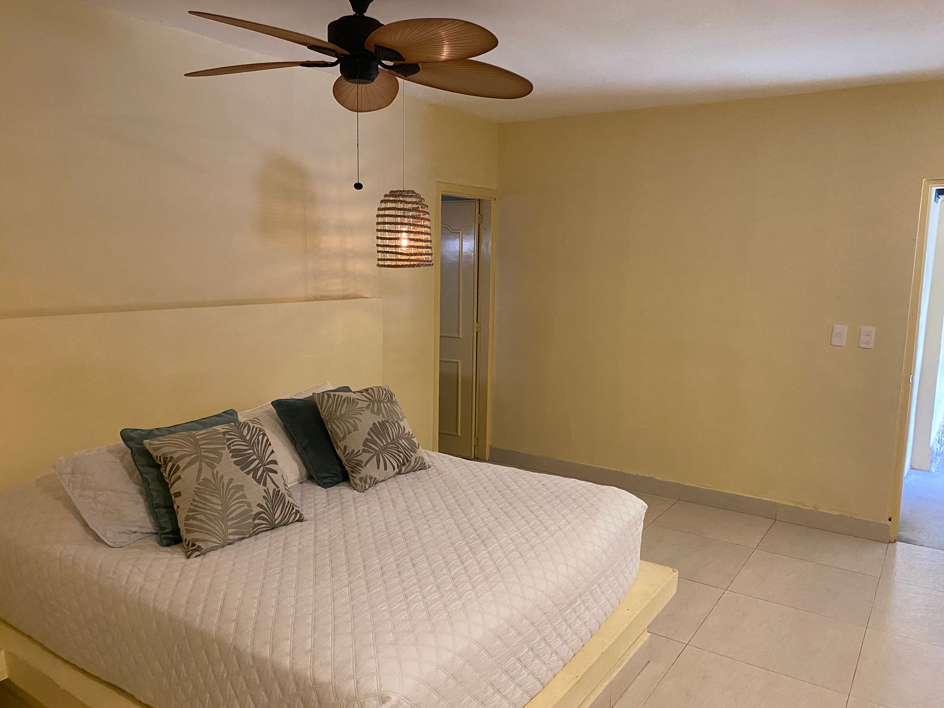 Bedroom with a white bed, beige walls, ceiling fan, and a woven pendant light.