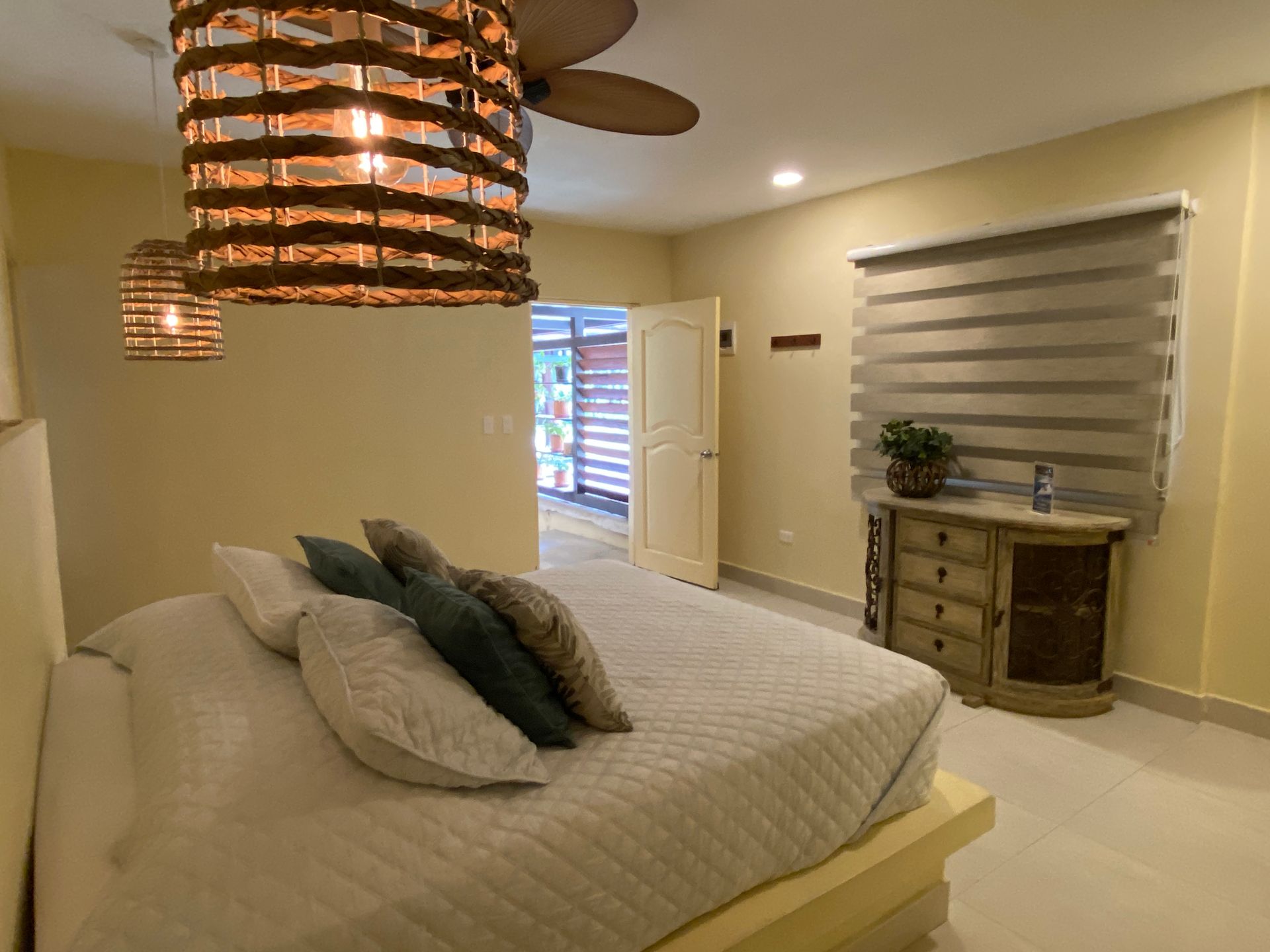 Bedroom with bed, dresser, window, and wicker pendant lights.