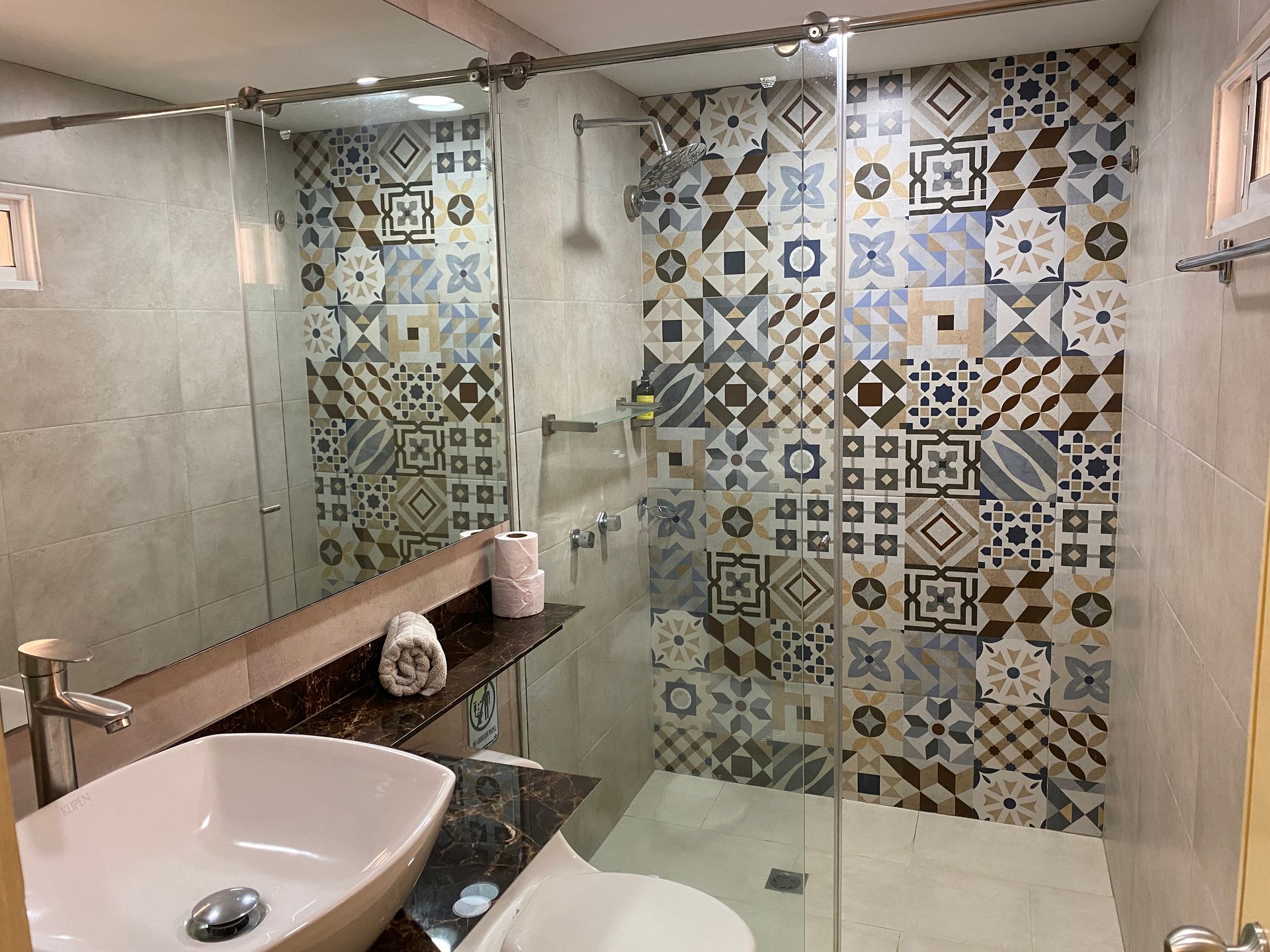 Bathroom with a patterned tile shower, glass door, and white sink.
