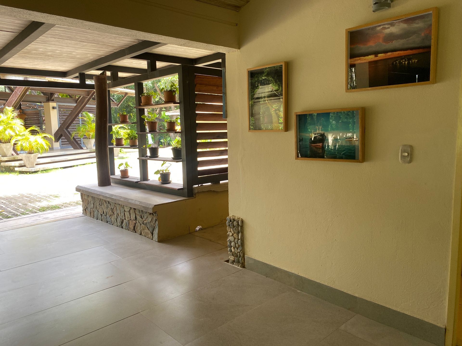 Indoor-outdoor space with artwork on wall, plants, and tiled floor. A shaded area with wood and stone features.