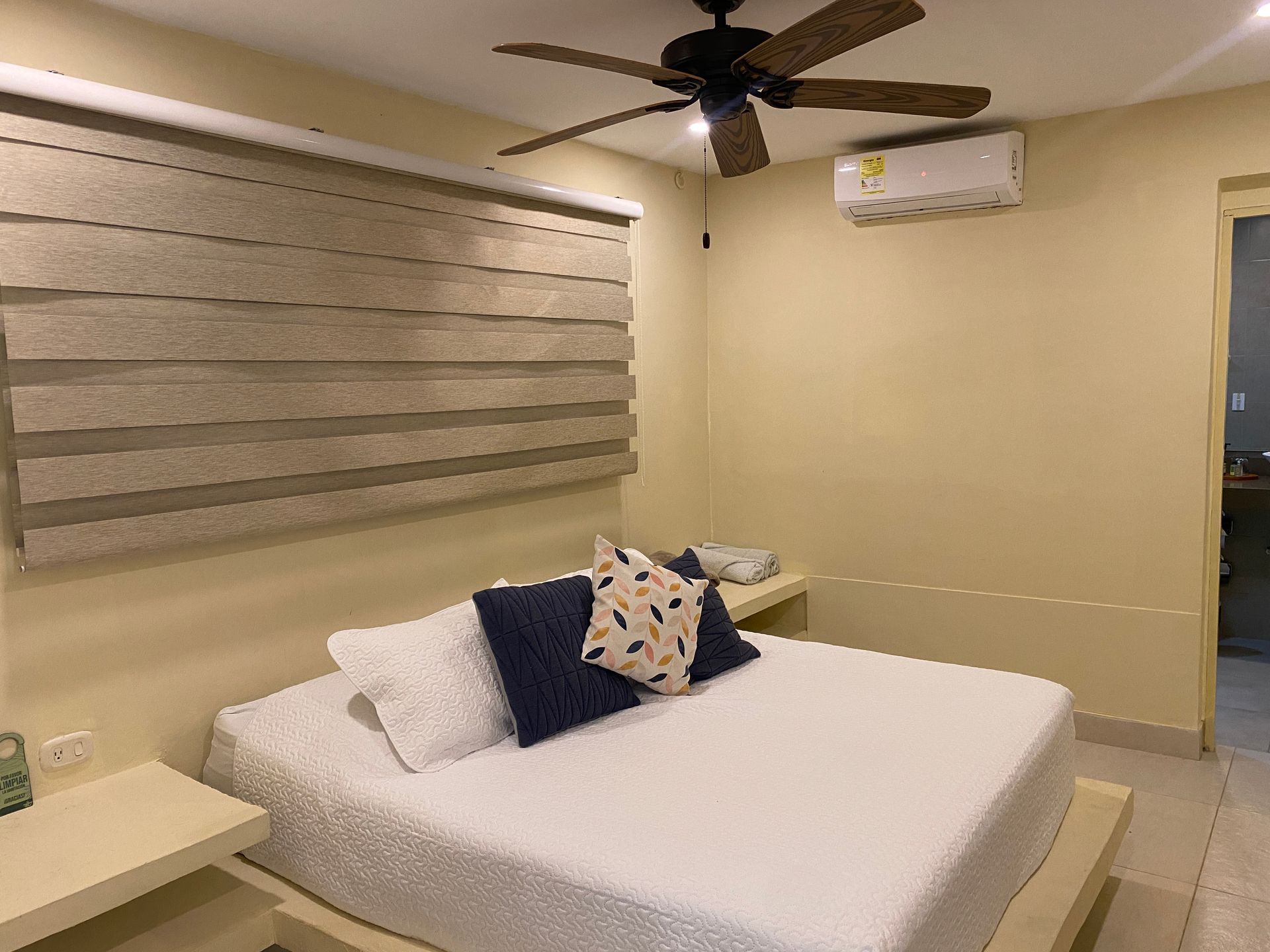 Bedroom with bed, pillows, window shade, ceiling fan, and air conditioner.