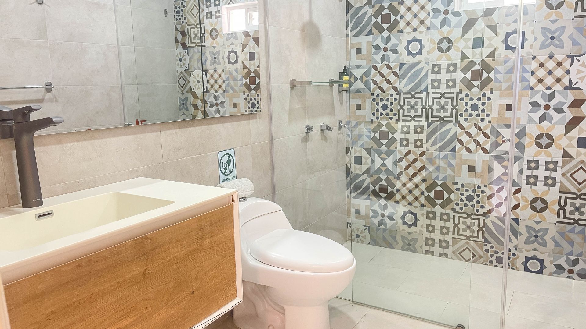 Bathroom with patterned tile wall, white toilet, wooden vanity, and large mirror.