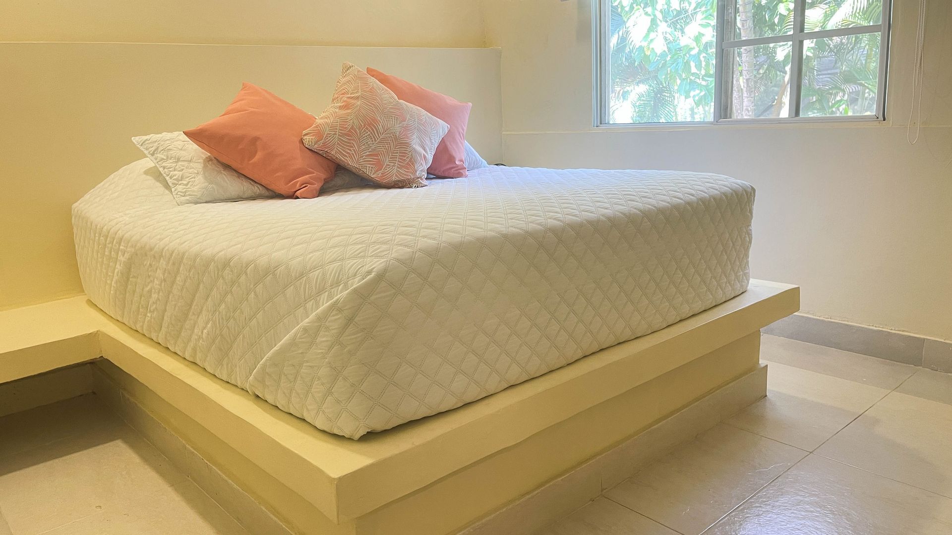 Cream-colored, heart-shaped bed with pillows, next to a window. Light yellow base, white floor.