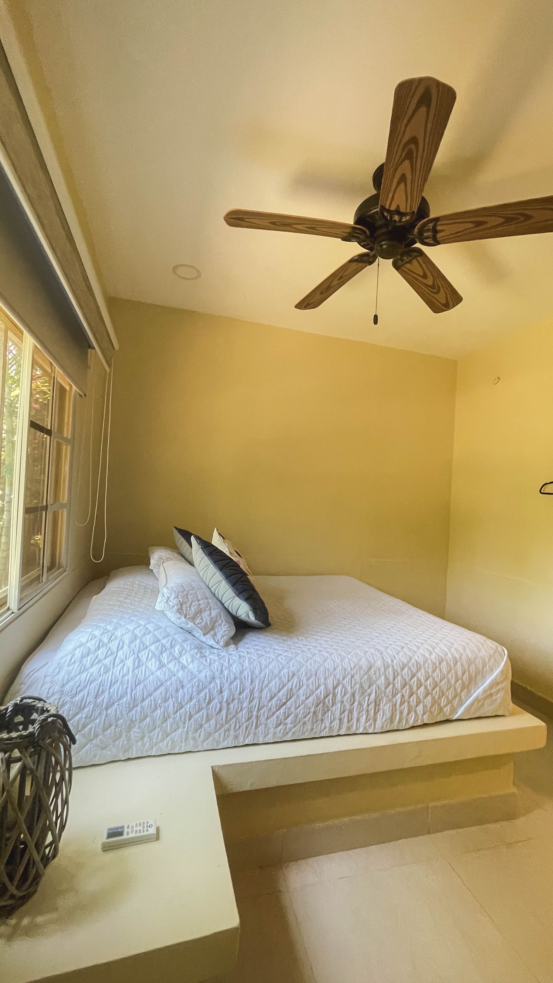 Bedroom with a low platform bed, pillows, and a wooden ceiling fan.