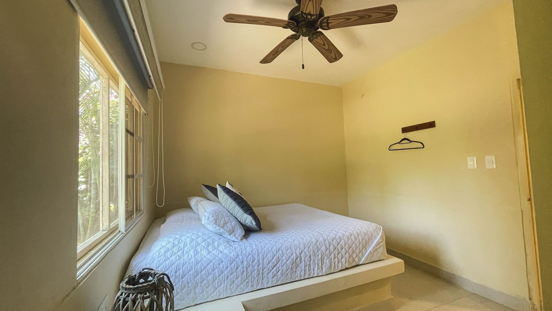 Bedroom with a bed, pillows, and a window. Ceiling fan and a coat hanger on the wall.