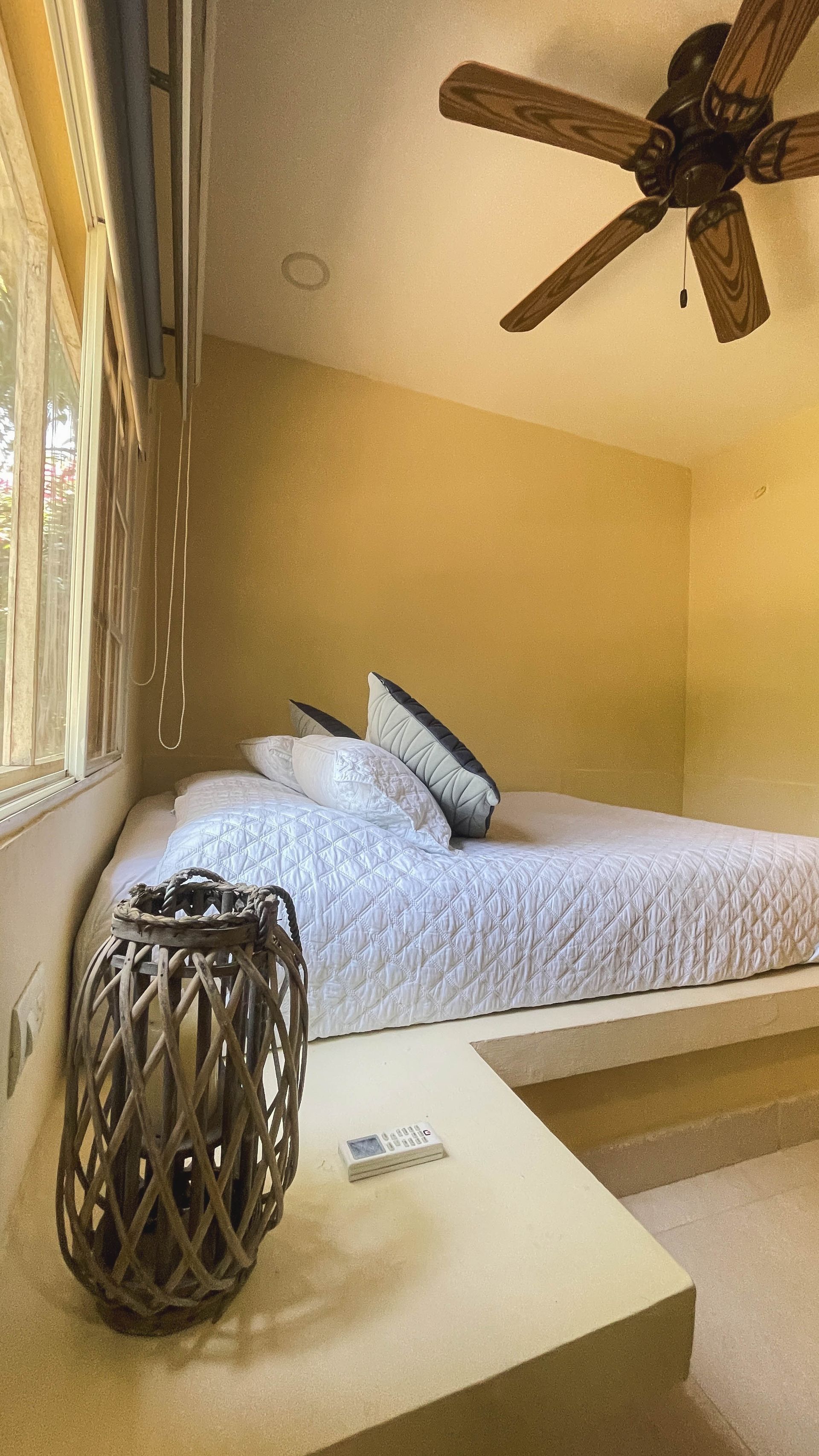 Bedroom with platform bed, tan walls, ceiling fan, wicker lantern, and patterned bedding.