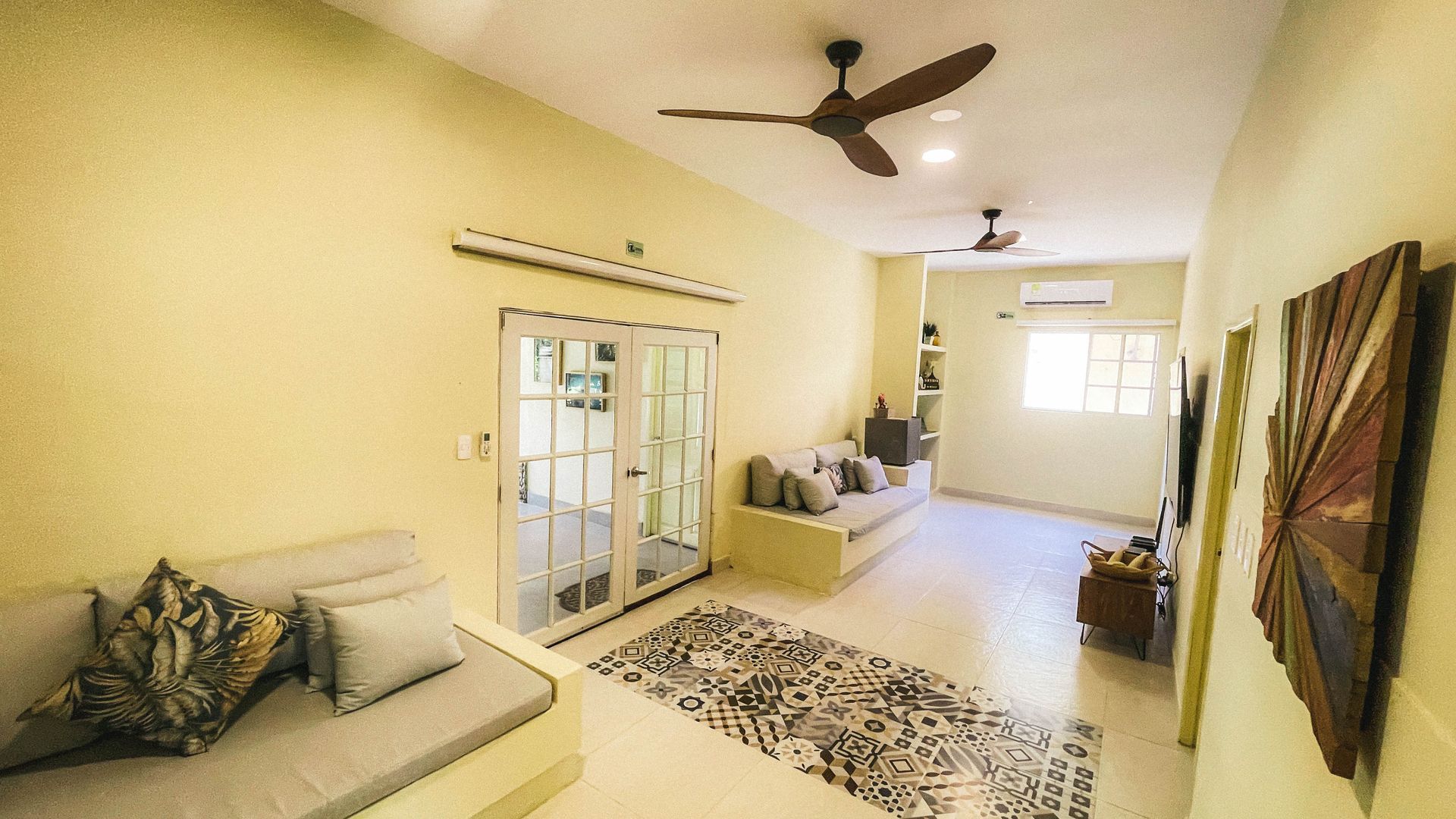 Living room with light yellow walls, two couches, rug, ceiling fans, and doorway to outside.