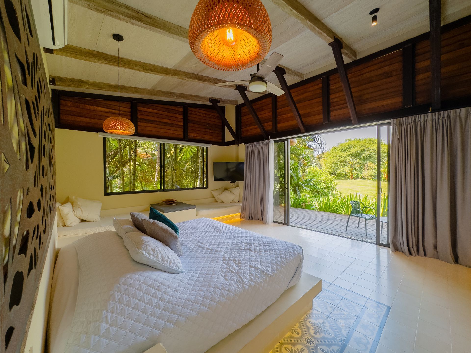 Bright bedroom with a white bed, open door to a green field, wooden beams, and pendant lights.