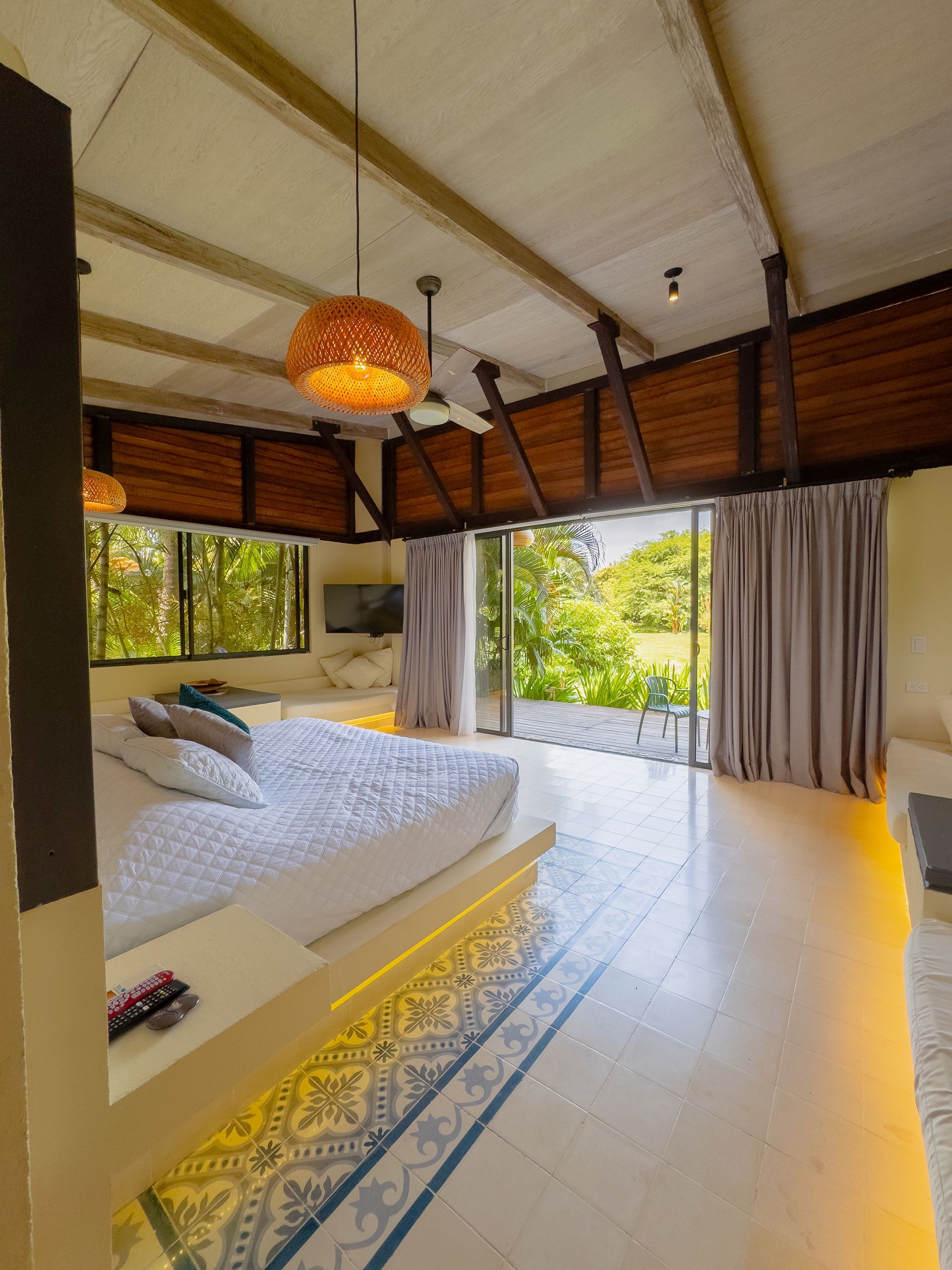 Spacious bedroom with white bed and wood accents, opening to a green outdoor view.