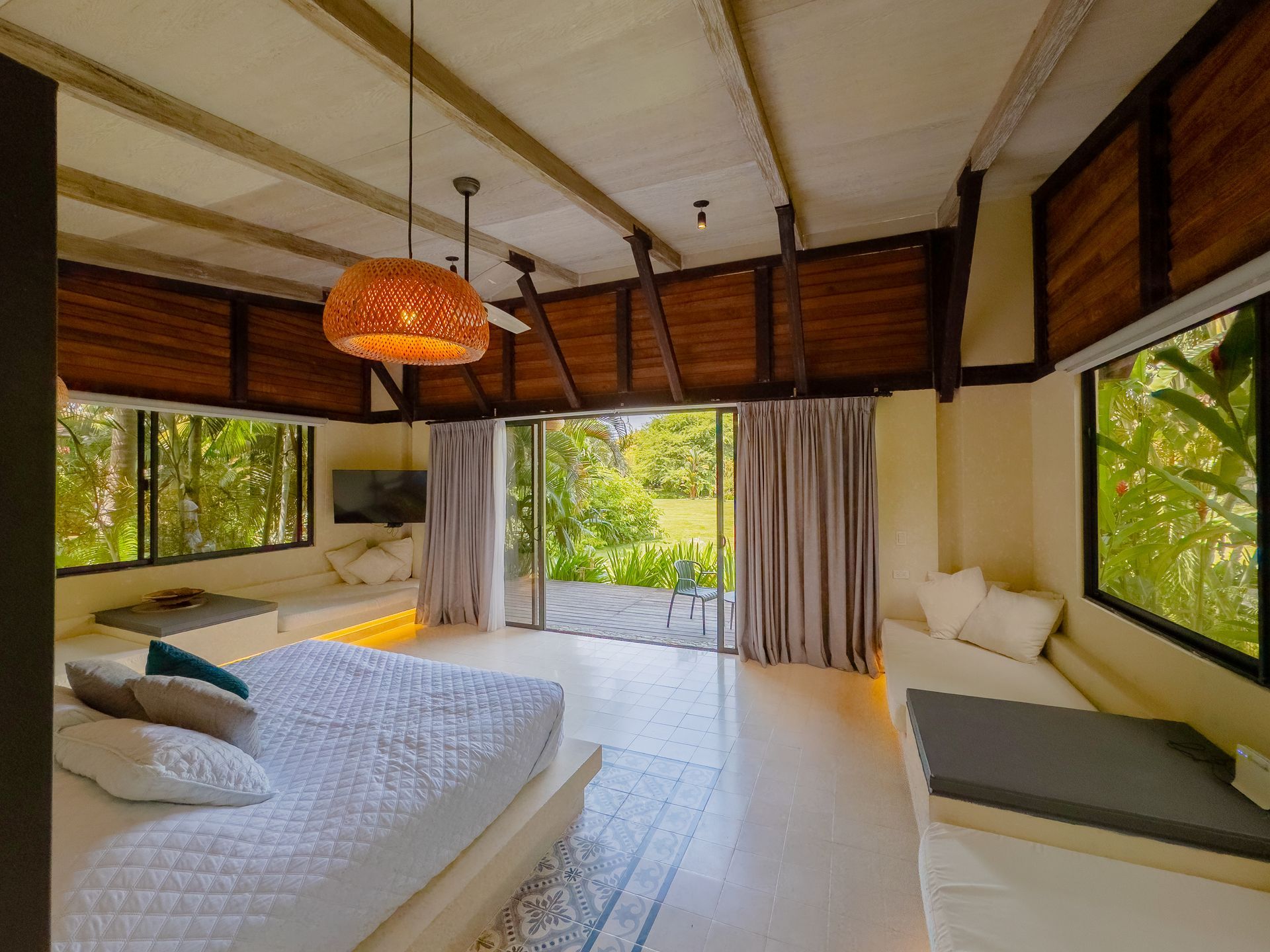 Bright bedroom with large bed, windows, and balcony opening to greenery.