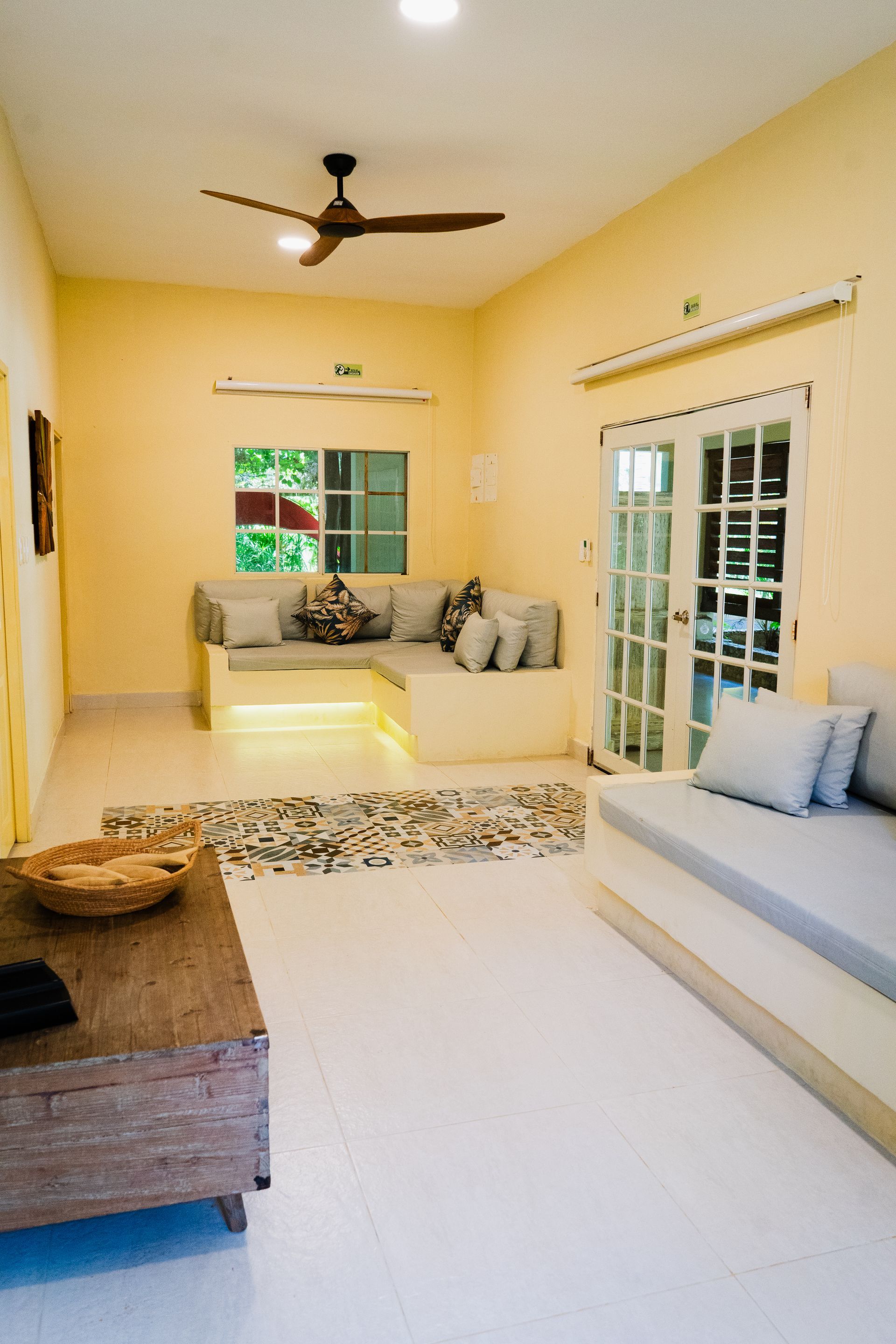 Living room with light yellow walls, beige couches, wood coffee table, and white floors.