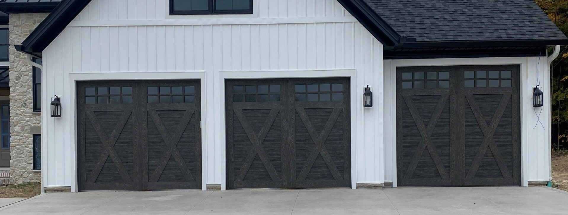 A white farmhouse with a three-car garage, featuring dark gray doors and black light fixtures.