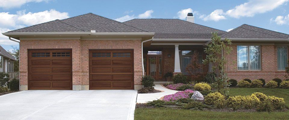Exterior view of a brick house with brown garage doors, a concrete driveway, and landscaping.