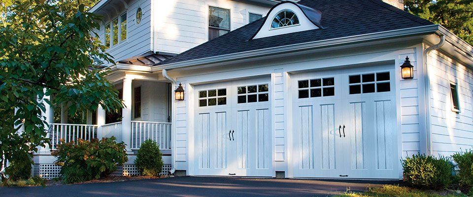 White house with white garage doors, black roof, and bushes.